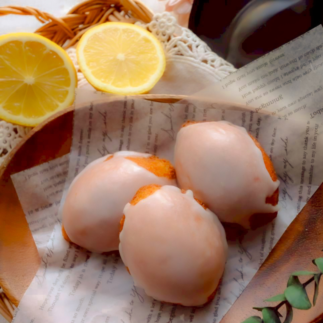 白いグレーズがかかった丸いレモンケーキ3個と、カットしたレモンが添えられた様子